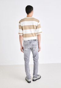 Randig kortärmad skjorta i beige och vit, tillsammans med ljusgrå jeans. Skjortan har en avslappnad passform, och jeansen har bakfickor.