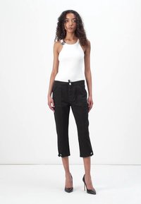Pantalones cortos negros con bolsillos frontales, que cuentan con un cierre de botón y detalles laterales. Combinados con una blusa blanca sin mangas y tacones negros.