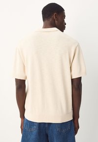 Cremefarvet kortærmet pullover med krave, ribstrikkede manchetter og kant, tekstureret strikket stof, der har en afslappet pasform og et minimalistisk design.