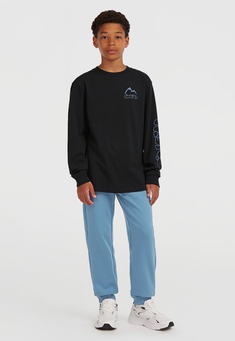 Langärmliges schwarzes Shirt mit blauem Logo, kombiniert mit hellblauen Sweatpants und weißen Turnschuhen, mit elastischen Bündchen an den Knöcheln.