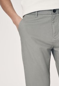 Pantaloni grigi con superficie testurizzata, taglio dritto e tasca anteriore. Presentano un bottone e passanti per cintura in vita.