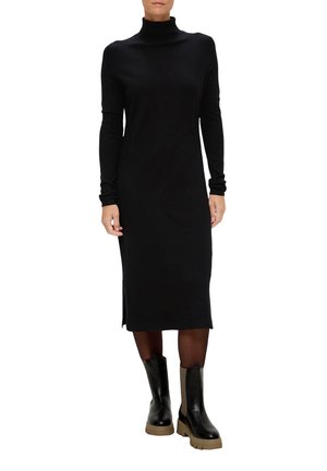 Zwarte coltrui jurk met lange mouwen, nauwsluitend model, zijsplitten, gemaakt van zacht materiaal. Gecombineerd met kniehoge zwarte en bruine chunky laarzen.