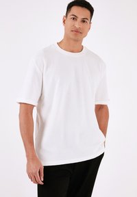 Tricou scurt cu mânecă albă, din bumbac, cu guler rotund și croială relaxată. Textură subtilă, cu manșete răsucite și tiv drept.