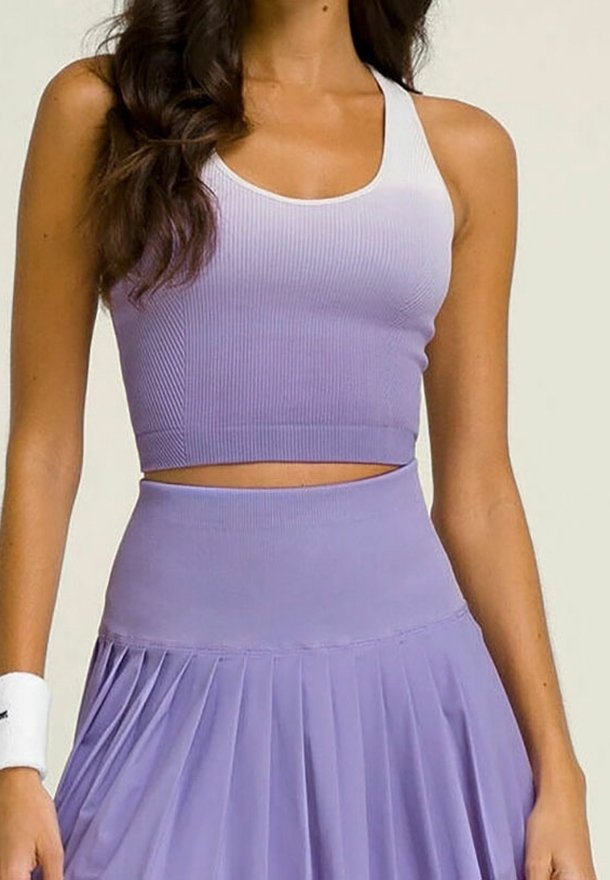Femme portant un haut court violet sans manches côtelé et une jupe plissée violette taille haute avec un bracelet blanc au poignet.
