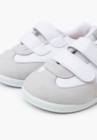 Grijze suède schoenen met witte leren accenten, voorzien van twee klittenbandsluitsingen en een gestructureerde, flexibele witte zool. Rondlopende neus.