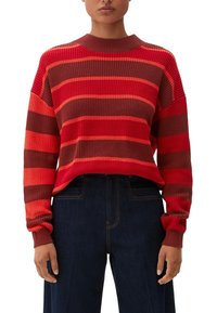 Rot- und braun gestreifter Pullover mit geripptem Material und rundem Halsausschnitt, kombiniert mit dunklen Jeans. Hat lange Ärmel mit enganliegenden Bündchen.