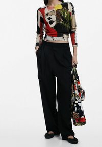 Haut en maille à motifs multicolores avec manches longues, taille haute, associé à un pantalon noir taille haute et un sac fourre-tout à motifs.