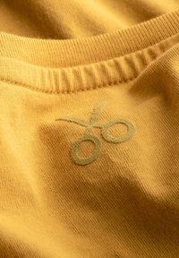Camicia di cotone gialla calda con un collo a costine e una grafica di forbici ricamata in un verde tenue. Tessuto morbido con un leggero lucido.