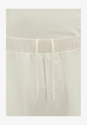 Pantalones color beige claro con tejido texturizado, cintura elástica con cordón y sutil patrón vertical. Diseño suave y casual.