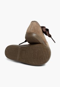 Zapatos de ante marrón con punta redonda, cordones decorativos de cinta y una suela de goma texturizada que presenta un patrón en forma de ola.