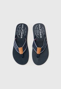 Flip-flops bleumarin cu o talpă din cauciuc texturat, curele din material și un accent din piele maro. Branding alb pe talpa interioară și pe curea.