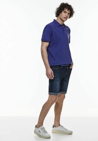 Camisa polo morada, pantalones cortos de mezclilla y zapatillas blancas. La camisa tiene cuello y los pantalones cortos están doblados en el dobladillo. Diseño casual, tejido ligero.