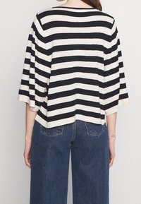 Pasiasta bluzka o luźnym kroju, z szerokimi rękawami i okrągłym dekoltem, w kremowym kolorze z granatowymi paskami. Zestawiona z dżinsami o wysokim stanie w niebieskim kolorze.