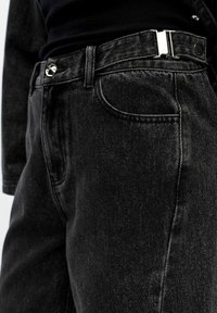 Black denim jeans with a slim fit, featuring a silver metal button, high waistband, and prominent pocket stitching.