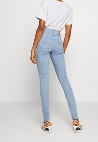 Jeans de tiro alto de color azul claro con un ajuste slim, que cuentan con dos bolsillos traseros y un parche de cuero con el logotipo en la cintura. Combinados con una camiseta gris.