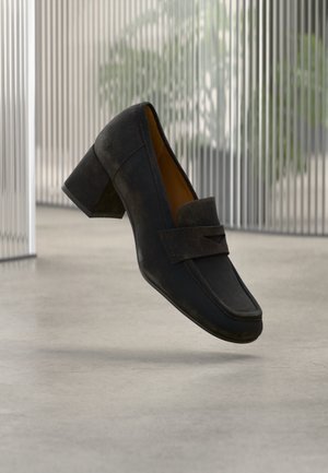 Čierna kožená topánka na vysokom podpätku s okrúhlou špičkou, ktorá má predný remienok a minimálne švy. Hladká textúra, zvýšený podpätok.