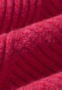 Gros plan sur un tissu tricoté rouge doux et duveteux avec des fibres de laine visibles et une texture côtelée dans différentes nuances de rouge.