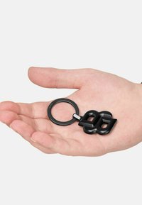 Black keychain featuring a bold, abstract design. Made of smooth plastic, consists of a circular ring and an outline of overlapping shapes.
