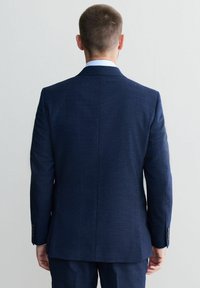 Sacou tailorat de culoare bleumarin, cu un finisaj texturat, guler deschis la culoare albastru și manșete cu nasturi; expus din spate.