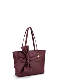 Bordeaux leren tote bag met een gestructureerde afwerking, voorzien van een grote strik aan één kant en twee schouderbanden. Inclusief een decoratieve hanger.