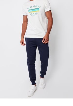 Witte T-shirt met een grafische print "Saint Tropez" en marineblauwe sweatpants. Outfit gecombineerd met witte sneakers, met een ontspannen pasvorm en geribbelde manchetten.