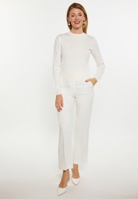 Pulover tricotat, ajustat, de culoare crem, cu mâneci lungi, combinat cu pantaloni albi cu talie înaltă și picior larg, purtați cu pantofi cu toc pointat albi.