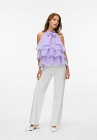 Lilla halter top koos kihiliste volangidega, võtmeauguga detail, paaritatud hõbedaste tekstuuriga laienevate pükste ja valgete plokknööpidega kingadega.
