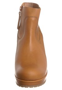 Bota de tobillo de cuero marrón con textura lisa, punta redonda y cremallera lateral. Presenta detalles de costuras y un tacón bajo y resistente.