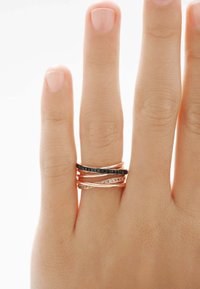 Anillos apilados con acentos en oro y negro, con diseños suaves y ondulados. Un anillo está adornado con pequeñas gemas transparentes.