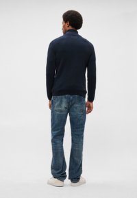 Ναυτικό πουλόβερ με ψηλό γιακά, εφαρμοστή σχεδίαση, σε συνδυασμό με ξεθωριασμένα μπλε τζιν και λευκά αθλητικά παπούτσια. Απαλή υφή, ελαφρύ ύφασμα.