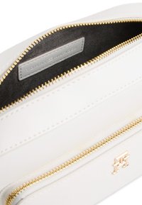 Λευκό δερμάτινο τσαντάκι με χρυστό φερμουάρ και λεπτομέρειες. Έχει γκρι ετικέτα εσωτερικά με ανάγλυφη την επιγραφή "TOMMY HILFIGER". Ομαλή υφή εξωτερικά.