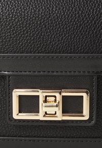 Borsa in pelle nera con texture, dotata di chiusura a lucchetto dorato e pannello frontale liscio con cuciture a contrasto. Eleganti accenti rettangolari.