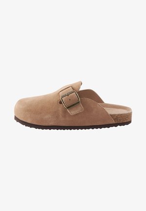Hellbrauner Wildleder-Slipper mit großer verstellbarer Schnalle und strukturierter dunkler Sohle, von der Seite auf weißem Hintergrund.