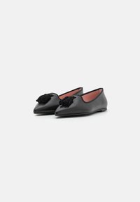 Svarta läderballerinas med spetsig tå, prydda med en dekorativ svart tofs framtill och en kontrasterande rosa insida.