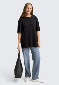 Zwart oversized T-shirt met subtiele studs, gecombineerd met lichtblauwe jeans en witte sneakers, aangevuld met een zwarte tote bag.