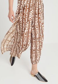 Pohodlné kalhoty hnědé a bílé barvy s geometrickými vzory, doplněné o protipólované checkered slip-on boty černobílé barvy se zlatými podpatky.