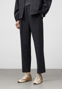 Donkergrijze op maat gemaakte broek met een rechte snit, met een gladde textuur en een subtiel patroon, gedragen met beige en crèmekleurige sneakers.