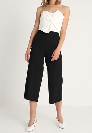 Biała bluzka bez ramiączek z teksturowanym skręconym wzorem, w połączeniu z czarnymi szerokimi, skróconymi spodniami i białymi wysokimi szpilkami.