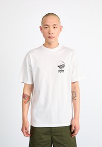 Hvid bomulds T-shirt med et lille sort grafisk print på brystet. Korte ærmer og rund halsudskæring.