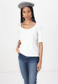 Hvid kortærmet top med rund halsudskæring, parret med blå jeans. Grå uldberet tilføjer tekstur. Simpelt, afslappet design.