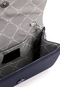 Otevřená tmavě modrá kabelka ve tvaru psaníčka ukazující šedou vzorovanou látkovou podšívku s prošitou kapsou a kovovým řetízkem s klipem uvnitř.