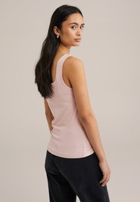 Top de tirantes anchos de color rosa claro con canalé, con un diseño ajustado y un dobladillo curvado, combinado con pantalones oscuros de cintura alta.