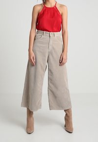 Top halter rosso abbinato a pantaloni beige in corda a gamba larga e stivali beige fino al ginocchio. Tessuto liscio e vestibilità rilassata.