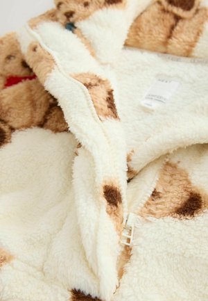 Mikina z fleecu v krémovej farbe s hnedými škvrnami. Predné zapínanie na zips a štruktúrovaná tkanina pre teplo a pohodlie.