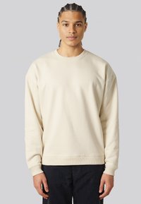 Felpa beige chiaro con collo a giro, spalle basse e polsini a costine. Realizzata in un tessuto morbido, presenta una vestibilità rilassata.