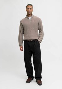 Suéter de cremallera beige de punto con una textura acanalada, combinado con pantalones negros de pierna ancha y zapatos marrones de cordones.