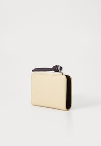 Portefeuille en cuir beige clair avec une surface texturée, doté d'une tirette de fermeture éclair violet foncé et d'une forme rectangulaire compacte.