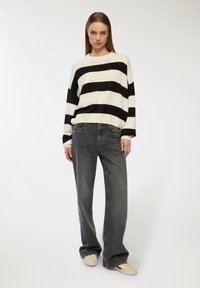 Czarny i biały sweter z dzianiny w paski, z okrągłym dekoltem, w zestawie z jasnoszarymi, luźnymi spodniami z wysokim stanem oraz beżowymi trampkami.