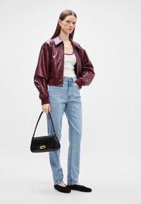 Μπουκάλα μπλούζα από τεχνητό δέρμα μπορντώ, λευκή αμάνικη μπλούζα, ανοιχτό μπλε ψηλόμεσα τζιν, μαύρη τσάντα χειρός με χρυσές λεπτομέρειες, μαύρα φλατ παπούτσια.