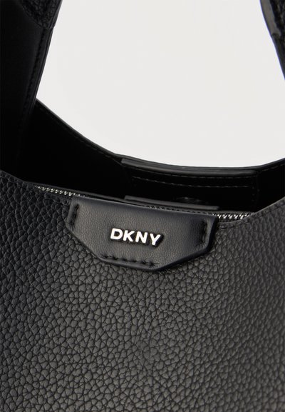 Черна текстурирана кожена чанта с сребристо лого на DKNY и видим цип вътре в основното отделение.